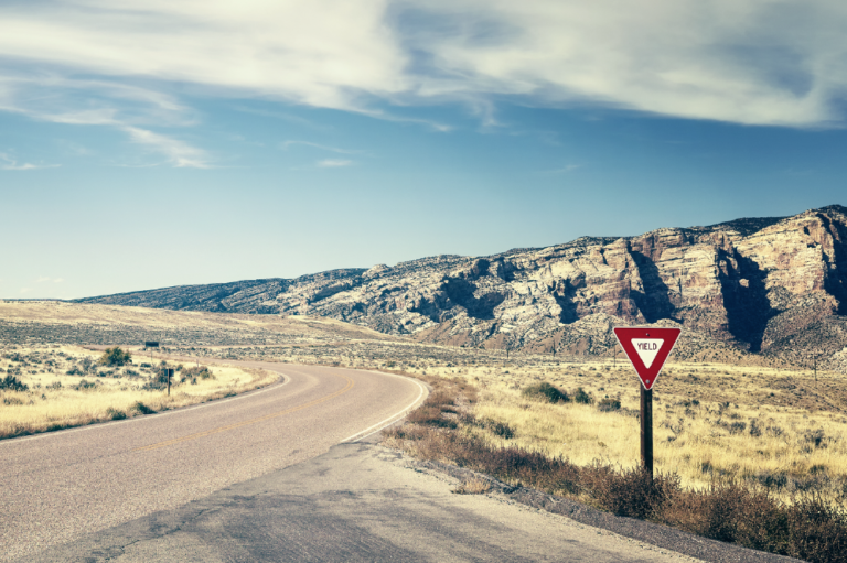 an open road through a desert with a 'yield' sign
