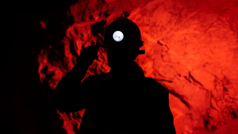 Silhouette of a man wearing a headlamp in a mine, with a red hue in the background