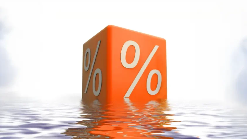 Large orange cube with % signs on each side, sitting atop a shallow body of water