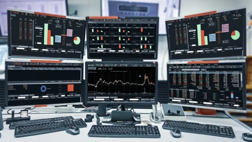 six computer screens set up at a desk, all showing financial data and charts